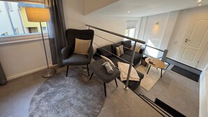 Ein modernes Wohnzimmer mit einem grauen Sofa, einem schwarzen Sessel und einem kleinen Tisch mit einer Lampe.