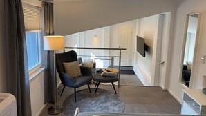 Ein modernes Schlafzimmer mit Bett, Stuhl, Nachttisch, Lampe, Fernseher und einem Fenster mit Vorhängen.