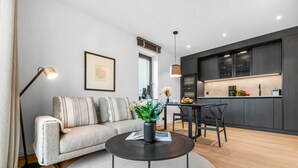 Uma sala de estar moderna com um sofá, uma mesa de centro e uma área de jantar com mesa e cadeiras. Há também uma cozinha com armários escuros e bancada.