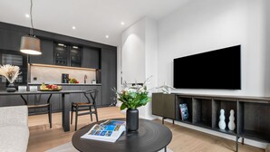 Uma sala de estar moderna com área de jantar, uma TV de tela plana na parede e uma cafeteira no balcão.