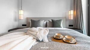 Quarto de hotel moderno com cama bem arrumada, duas luminárias laterais e bandeja de café da manhã com tigelas e colher.