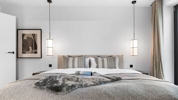 Quarto moderno com cama grande, duas luminárias pendentes, uma obra de arte emoldurada e vista para o exterior.