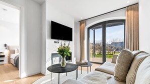 A modern living room with a large TV, a sofa, a coffee table, and a view of the outdoors. - Manhattan Suit – New Luxury Spread Across 2 Floors with Finnish & Infrared Sauna (List auf Sylt)