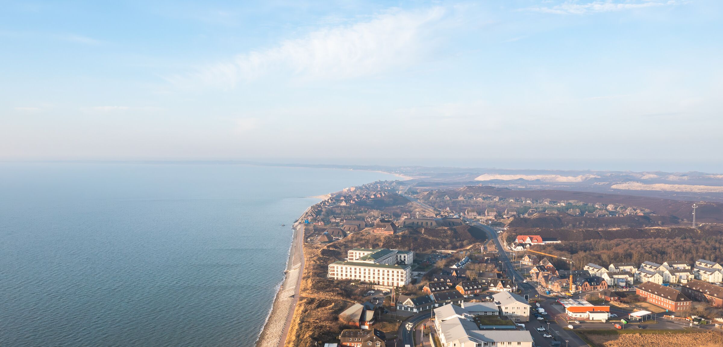 Vista aérea de un pueblo costero con playa, edificios y una carretera que lleva a una ciudad más grande.