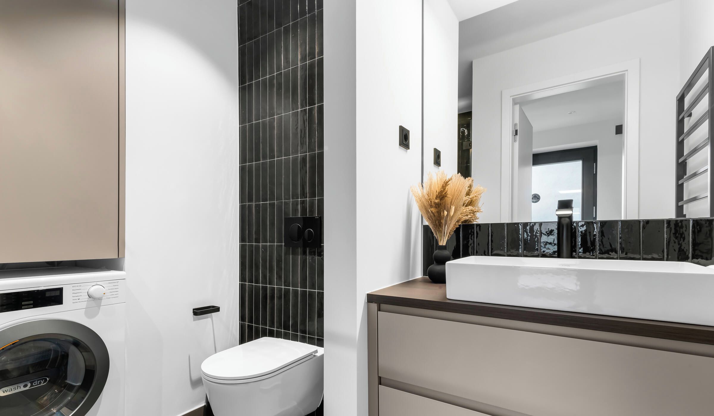 A modern bathroom with a washing machine, a toilet, and a sink with a mirror above it.