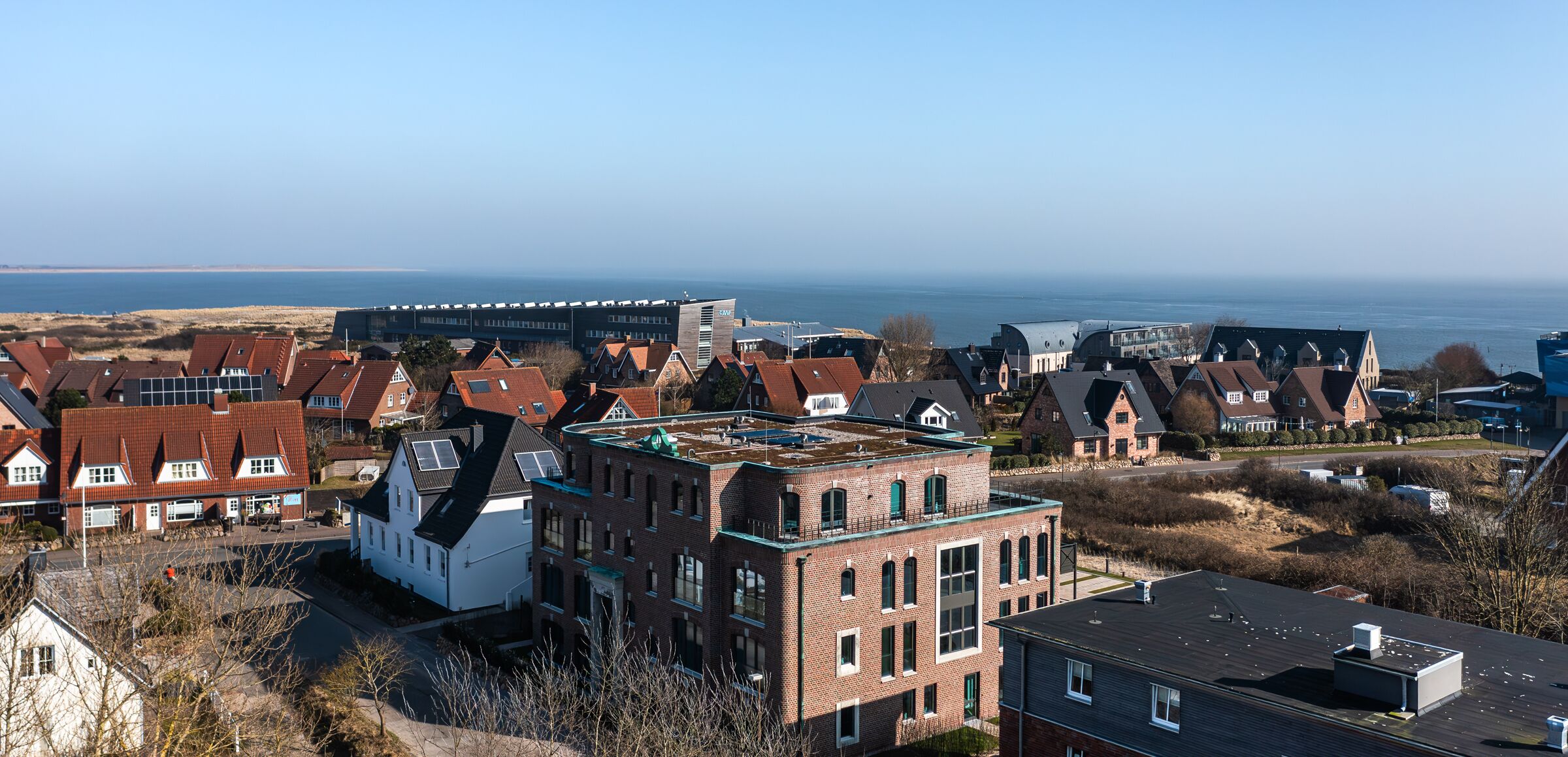 Een woonwijk met huizen, een groot gebouw met plat dak en uitzicht op zee.
