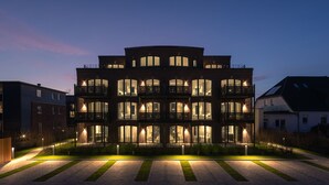 A multi-story building with balconies and large windows, surrounded by a well-maintained lawn and pathway.