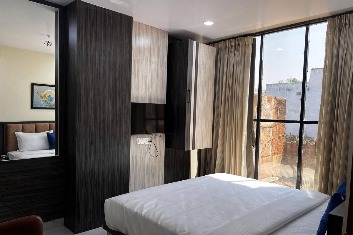 A hotel room with a large bed, a TV mounted on the wall, and a window with curtains.