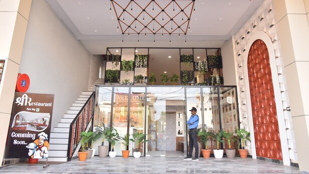Der Eingang des Soumya Sarovar mit einer Treppe, Topfpflanzen und einem Schild, das auf ein zukünftiges Restaurant hinweist.