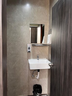Un baño con un lavamanos blanco, un secador de manos y un perchero para toallas.