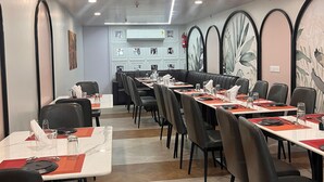 Ein Restaurant mit modernem Ambiente, das lange Tische mit schwarzen Stühlen, weiße Tischdecken und rote Platzsets bietet.