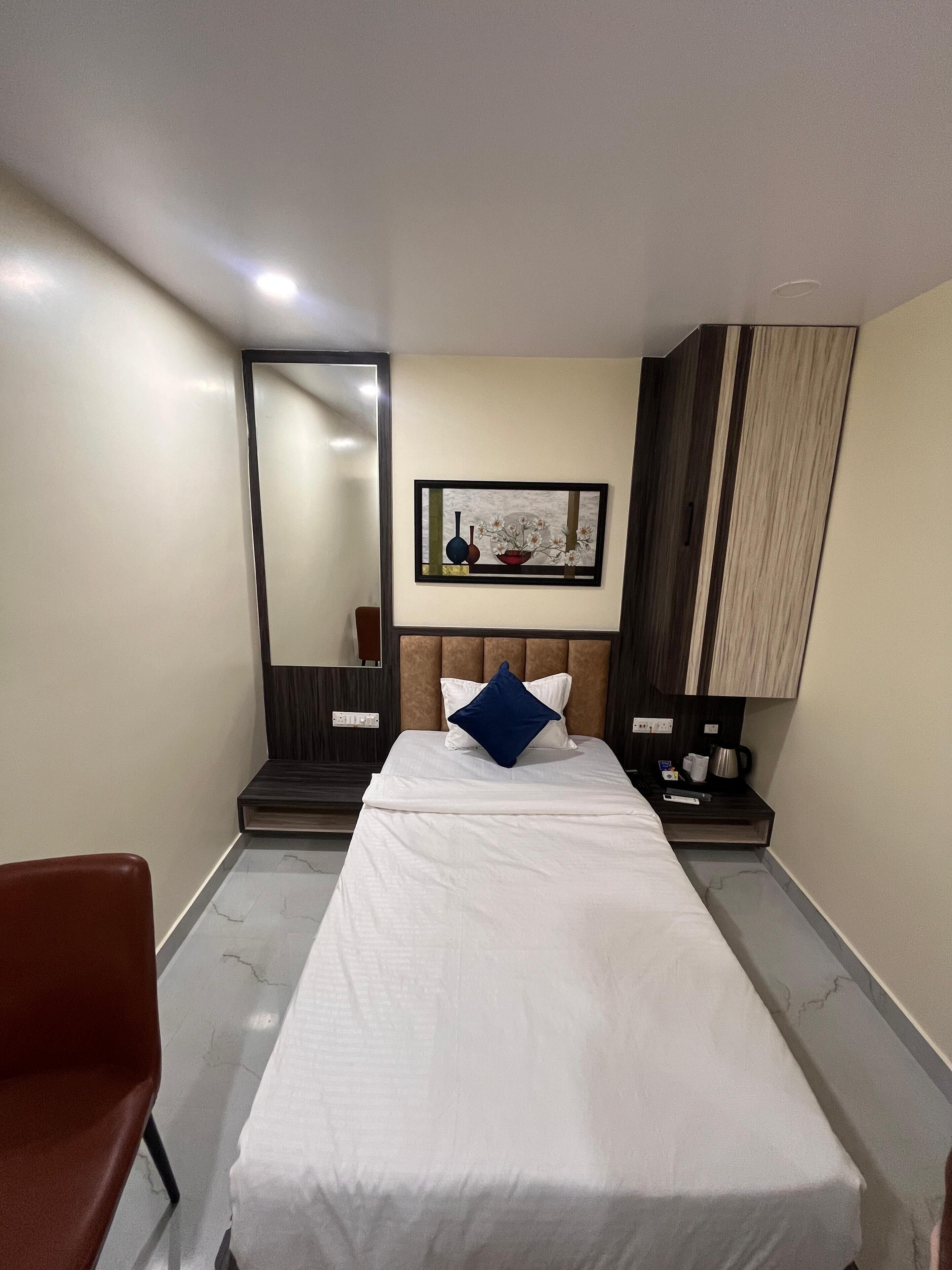 A hotel room with a bed, a chair, a nightstand, a coffee maker, and a framed picture on the wall.