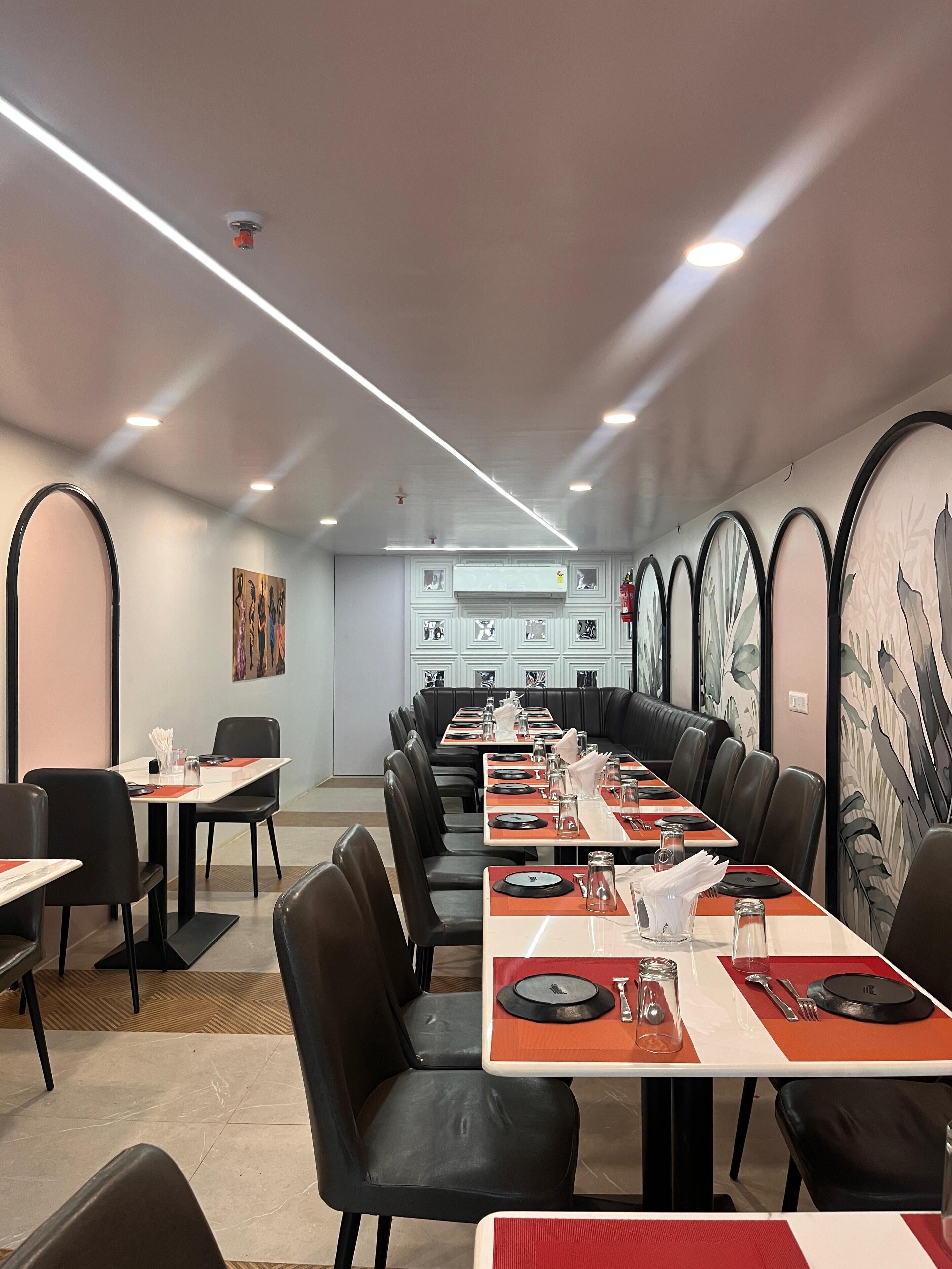 Un restaurant doté d’une longue table conviviale, de tables individuelles, de chaises en cuir noir et d’un design moderne au niveau du plafond.