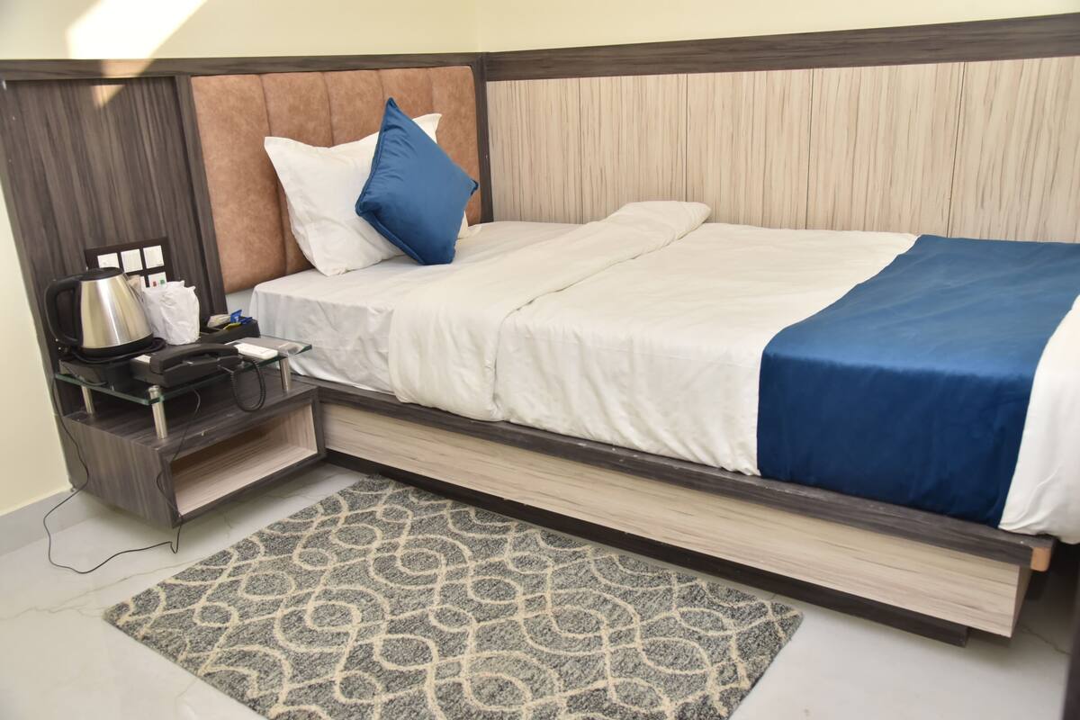 A modern hotel room with a bed, a nightstand, a coffee maker, and a patterned rug.