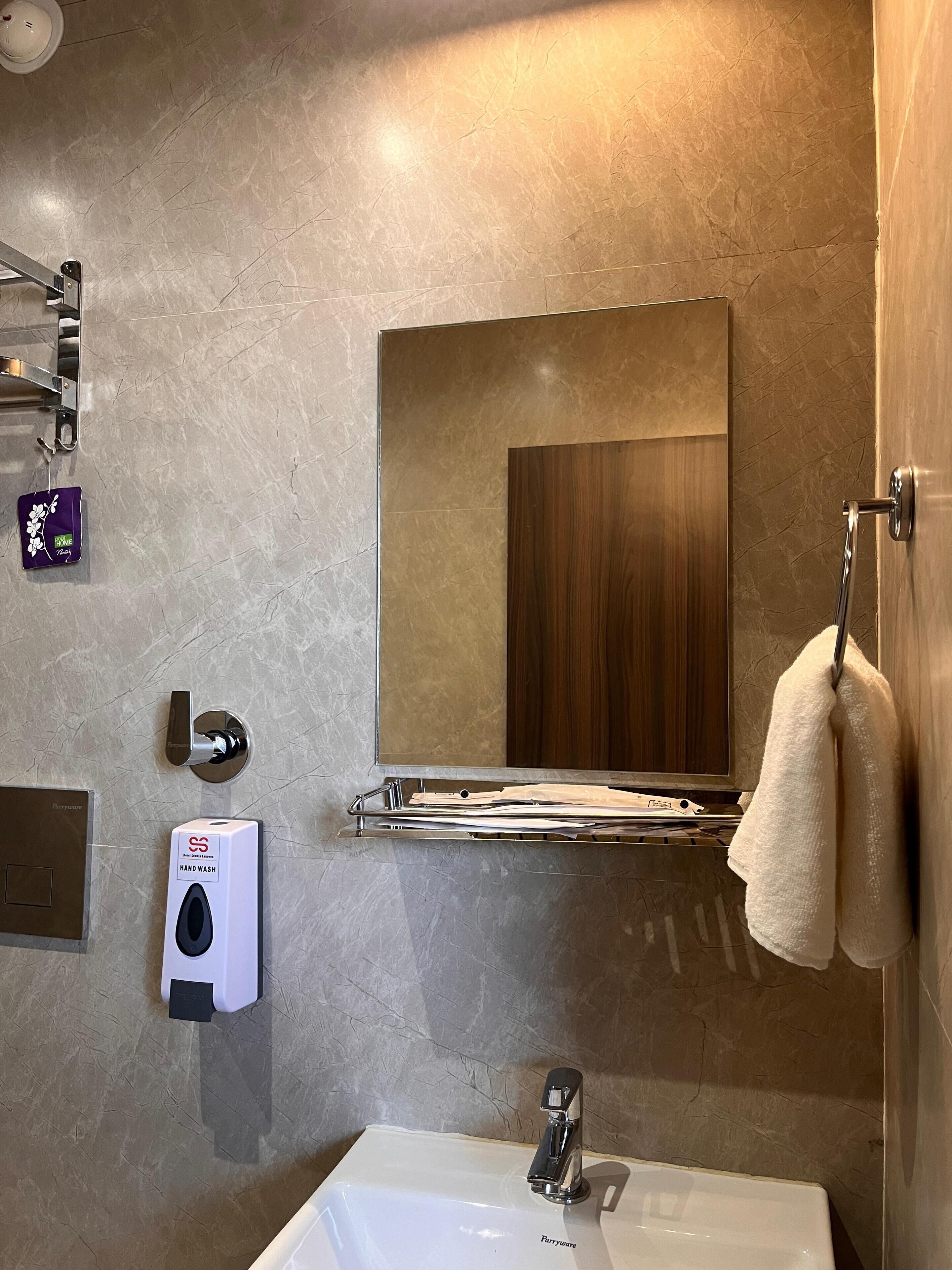 Un baño moderno con pared de mármol, un lavamanos, un perchero para toallas y un espejo.