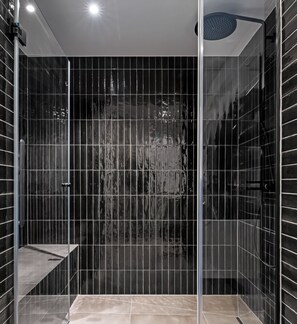 Un box de ducha moderno con puerta de cristal, un asiento integrado y un cabezal de ducha manual.
