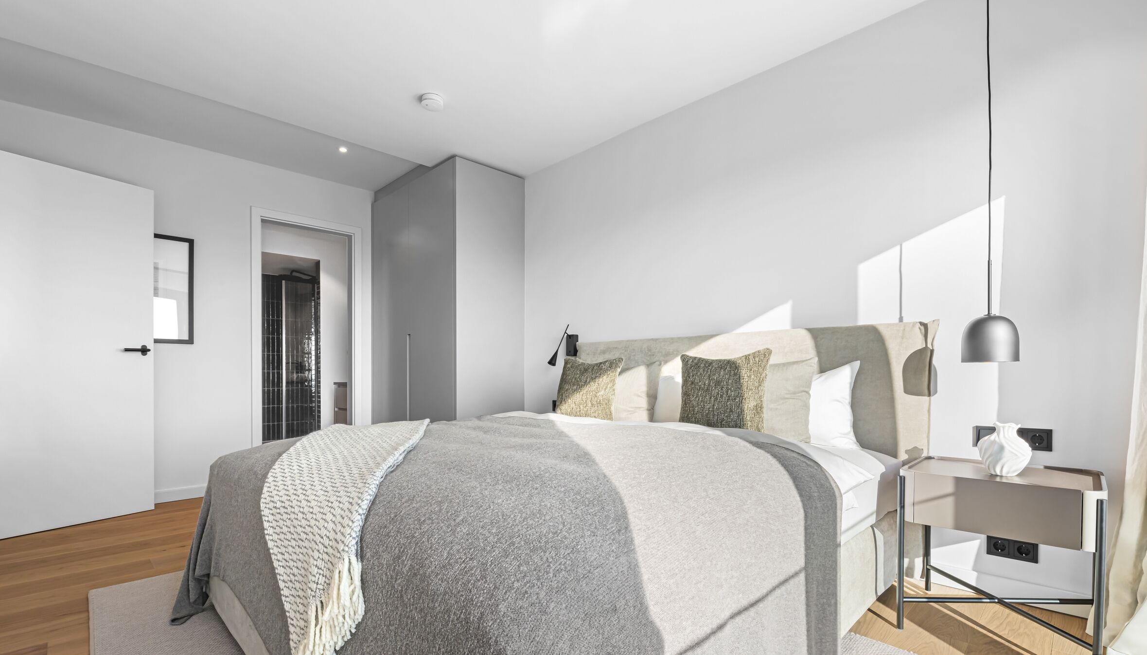 Een moderne slaapkamer met een groot bed, nachtkastje en een hanglamp.