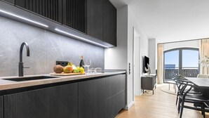 Une cuisine moderne avec des meubles de couleur bois foncé, un robinet noir élégant et un plan de travail en marbre. On y trouve un panier de fruits contenant des bananes, des raisins et une noix de coco, ainsi que des verres à vin et une bouteille.