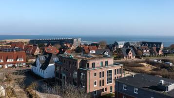 A residential area with houses, a large building with a flat roof, and a view of the sea.