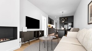 Un salon moderne avec une cheminée, un téléviseur à écran plat, un canapé et un coin repas, avec une cuisine en arrière-plan.