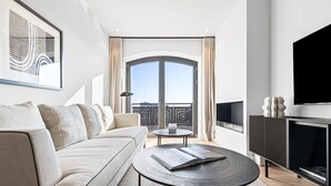 Un salon moderne comprenant un canapé, une table basse, une cheminée, un téléviseur et une grande fenêtre avec des rideaux.