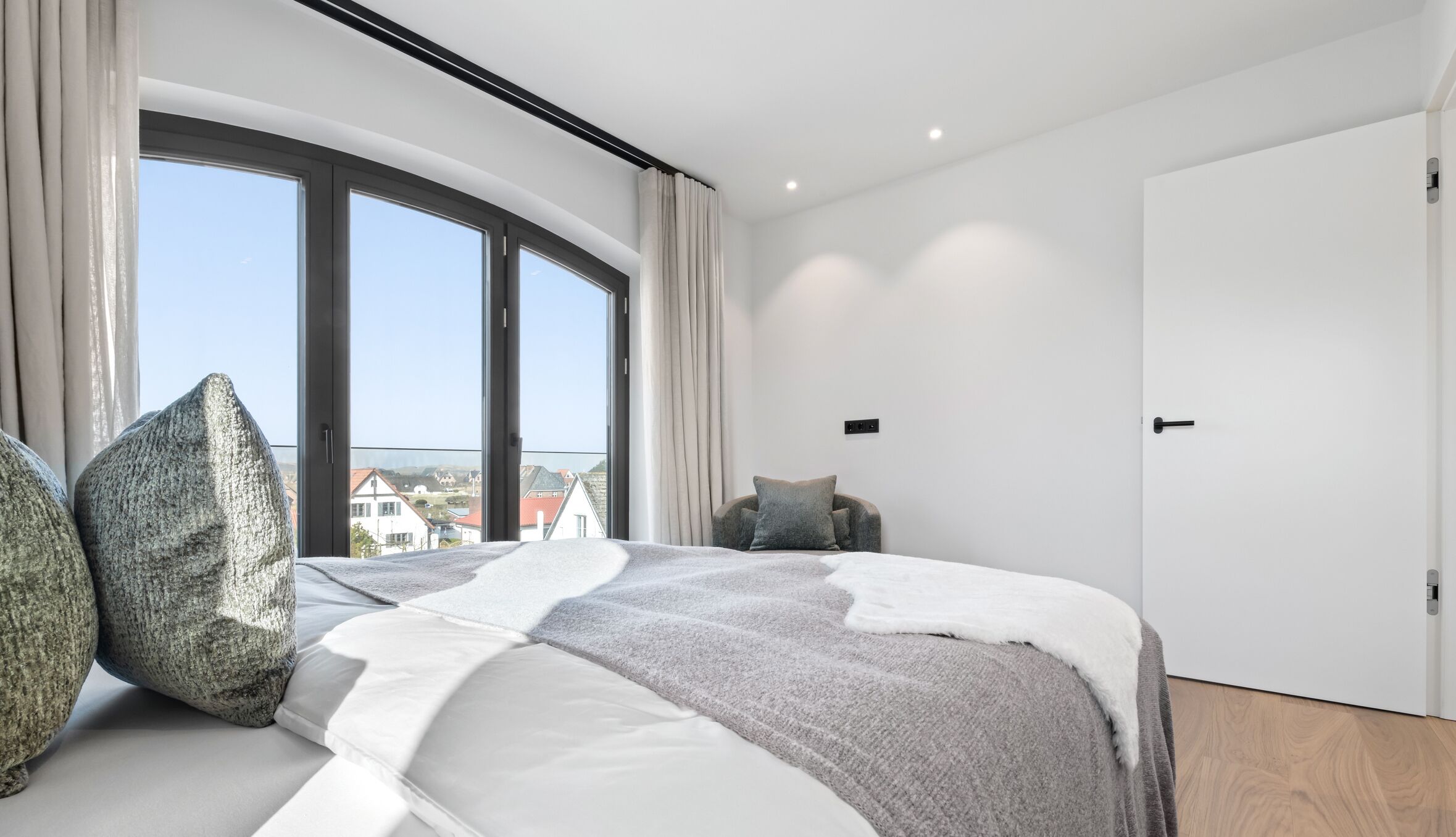 A modern bedroom with a large bed, a view of the outside, and a white door.