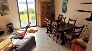 Ein Essbereich mit Tisch und Stühlen, einem Schrank und Blick auf ein Gewässer durch eine Glastür.
