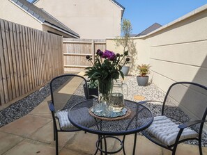Eine Terrasse mit zwei Metallstühlen, einem runden Tisch, einer Blumenvase und Topfpflanzen.