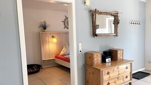 A room with a bed, a wooden dresser, a mirror, and a wall-mounted coat rack. - Your Perfect Getaway: Cozy Holiday Home in the Tranquil Countryside! (Rodenäs)