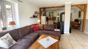 A living room with a brown sofa, a wooden coffee table, and a kitchen in the background. - Your Perfect Getaway: Cozy Holiday Home in the Tranquil Countryside! (Rodenäs)