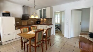 A compact kitchen with white cabinets, a microwave, and a dining area with a wooden table and chairs. - Your Perfect Getaway: Cozy Holiday Home in the Tranquil Countryside! (Rodenäs)