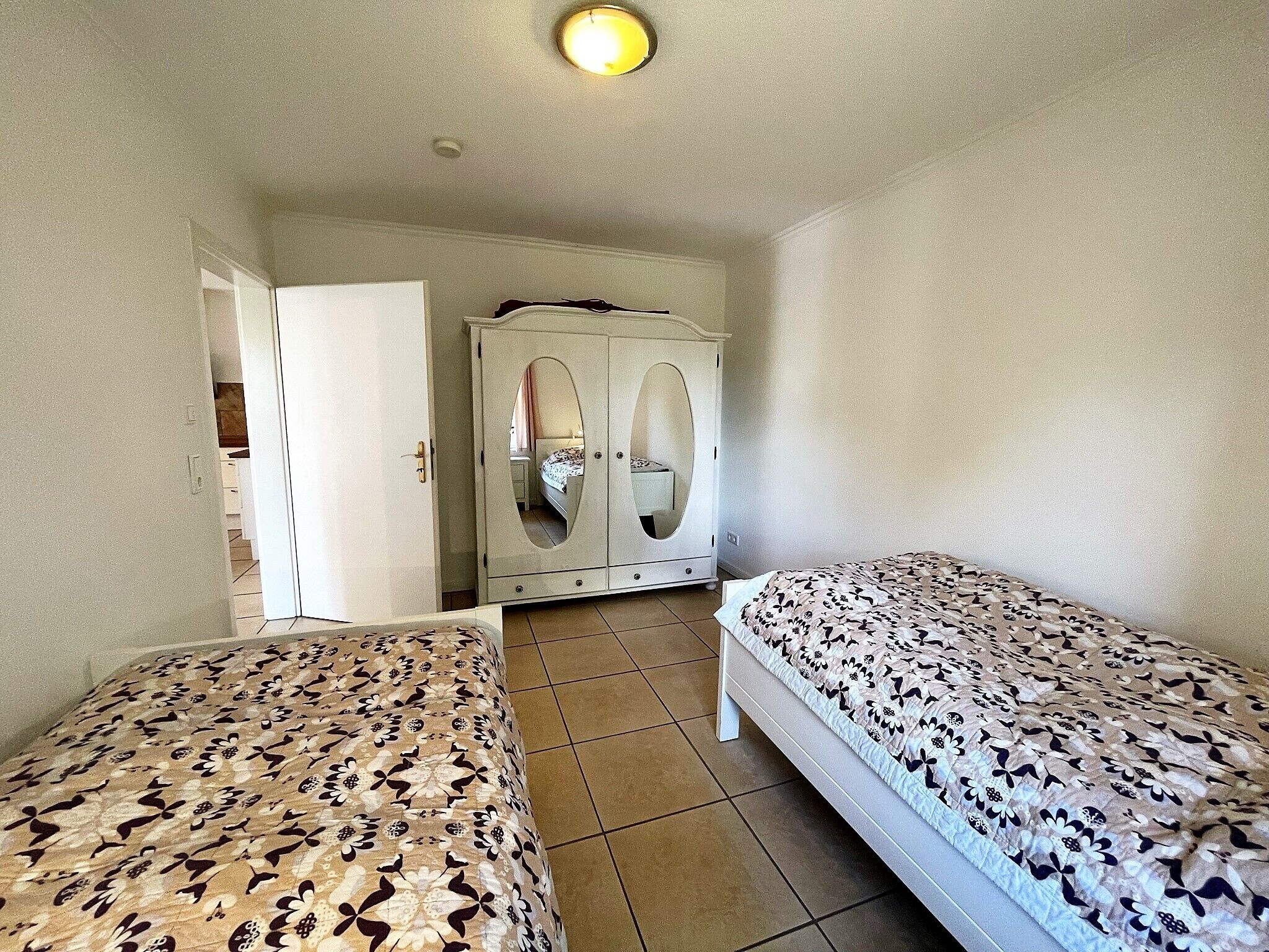 A bedroom with two beds, a wardrobe, and a bathroom visible through an open door.