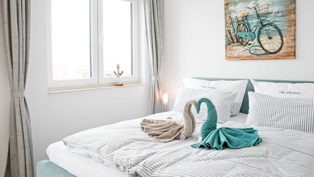 A neatly made bed with striped bedding, a teal towel, and a swan-shaped pillow. - Modern penthouse (55 sqm) open all year round for 2 to 4 people in the Staffel (Norderney)