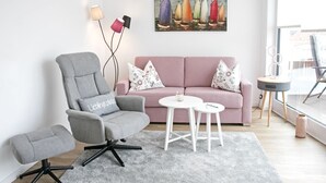 A modern living room with a grey armchair, a pink sofa, and a small white table. - Modern penthouse (55 sqm) open all year round for 2 to 4 people in the Staffel (Norderney)