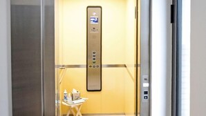 An elevator with a control panel, a small table with a chair, and a rug leading to the elevator.