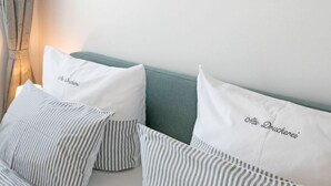 A bedroom with a bed, striped pillows, a teal headboard, and a beach scene painting on the wall.