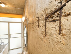 A bathroom with a bathtub, a window, and a wall with a textured surface and a wooden beam. - Standby Generator Bunker (Dorchester)