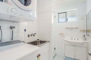 A modern bathroom with a built-in washing machine, a sink, and a mirror. - Absolute Beachfront Apartment 3T (Lennox Head)