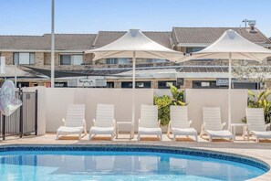 Una piscina con sillas de descanso y sombrillas, un edificio con techo de tejas y un letrero que dice 'baker'.