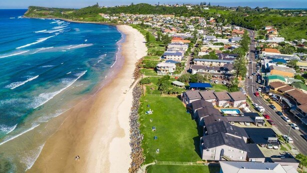An aerial view of a coastal residential area with houses, a beach, and a clear sky. - Absolute Beachfront Apartment 8B - 1 bedroom (Lennox Head)