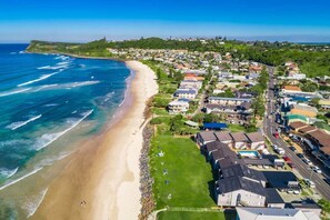 Vue aérienne d’une zone résidentielle côtière, avec des maisons, une plage et un ciel dégagé.