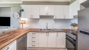A modern kitchen with white cabinets, a wooden countertop, a stainless steel sink, and a built-in oven.
