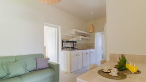 Une cuisine moderne avec des meubles blancs, un coin repas avec une table dressée pour quatre personnes, et un canapé vert agrémenté de coussins.