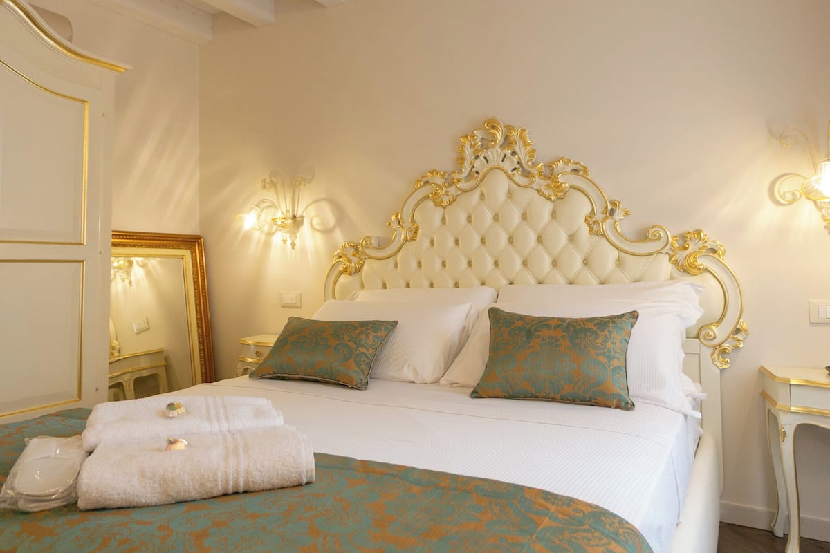 A bedroom with a large bed, a decorative headboard, bedside tables, and wall sconces.