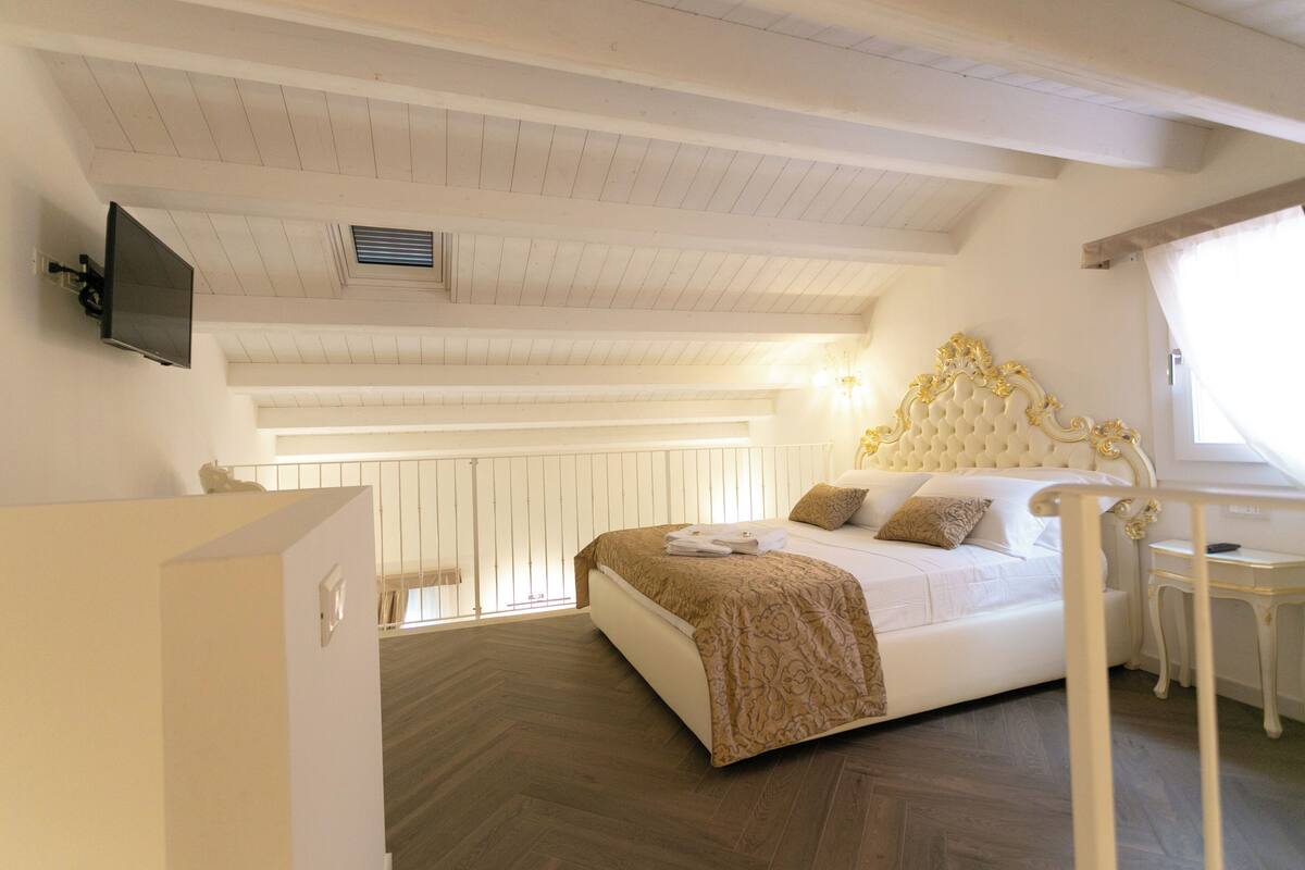 A bedroom with a large bed, a television mounted on the wall, and a window with curtains.