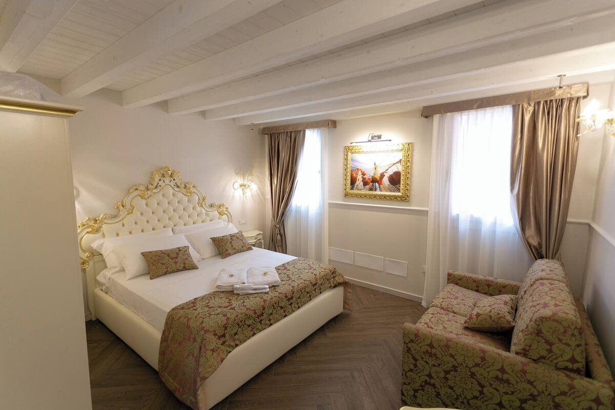 A bedroom with a large bed, a sofa, a chandelier, and a framed picture on the wall.