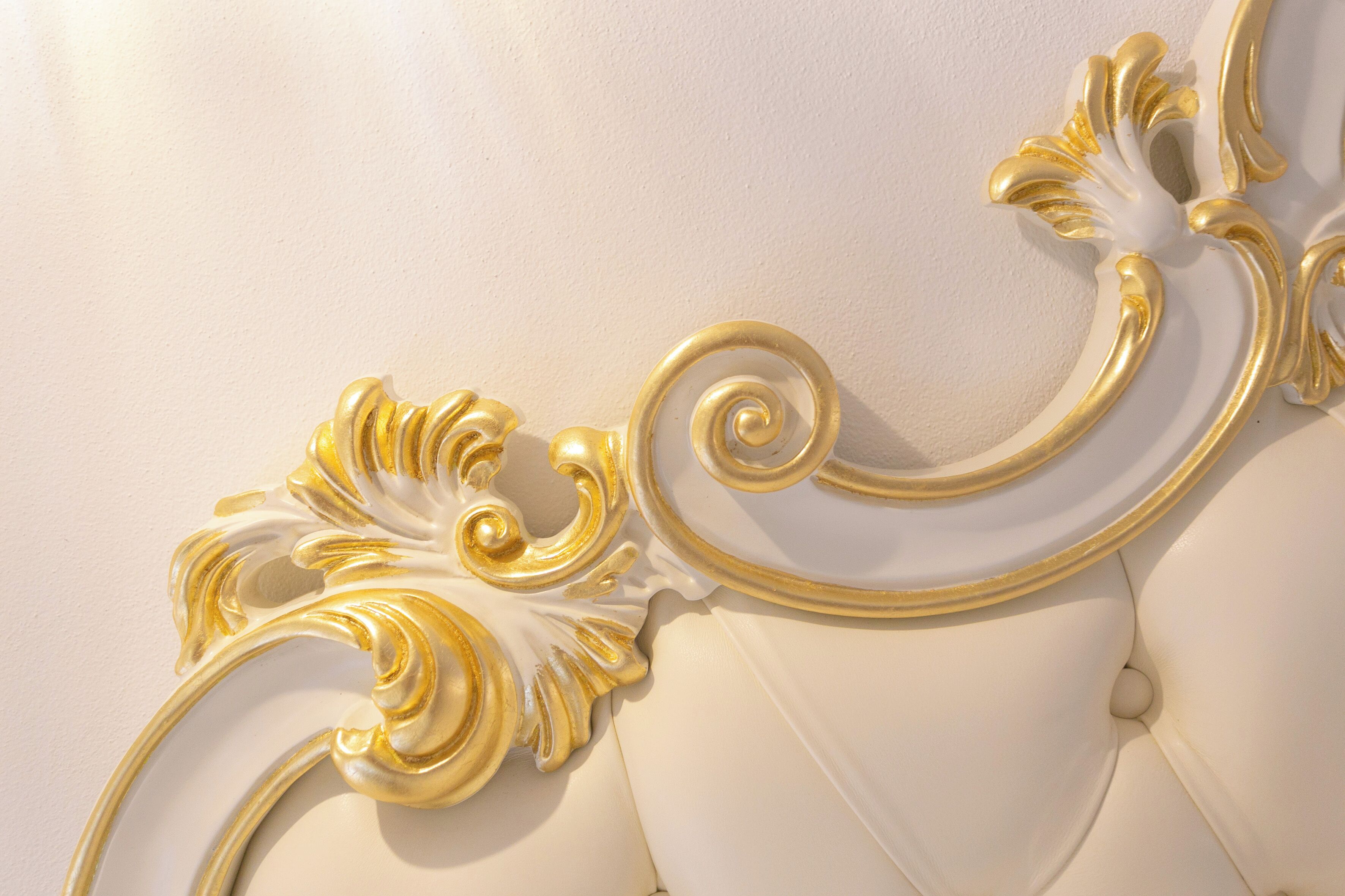 Primer plano de un cabecero blanco con detalles ornamentales dorados.