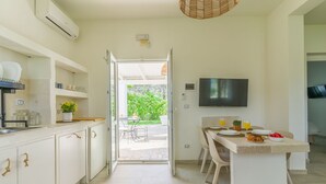Une cuisine moderne avec des meubles blancs, un coin repas avec une table dressée pour deux personnes, et un téléviseur fixé au mur.