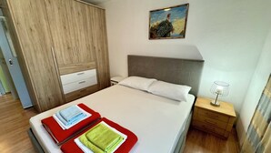 A hotel room with a bed, a nightstand, a lamp, a painting on the wall, and a wardrobe. - Apartment Fruk 5 (Jadranovo)