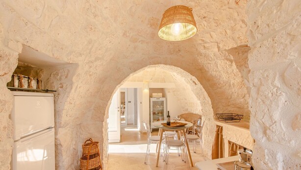 Uma cozinha rústica com um arco de pedra, uma geladeira, uma cesta de vime e um espaço de refeições com cadeiras e uma mesa.